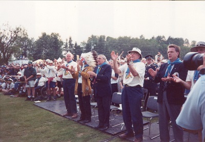 A line of men standing clapping with some wearing regalia 