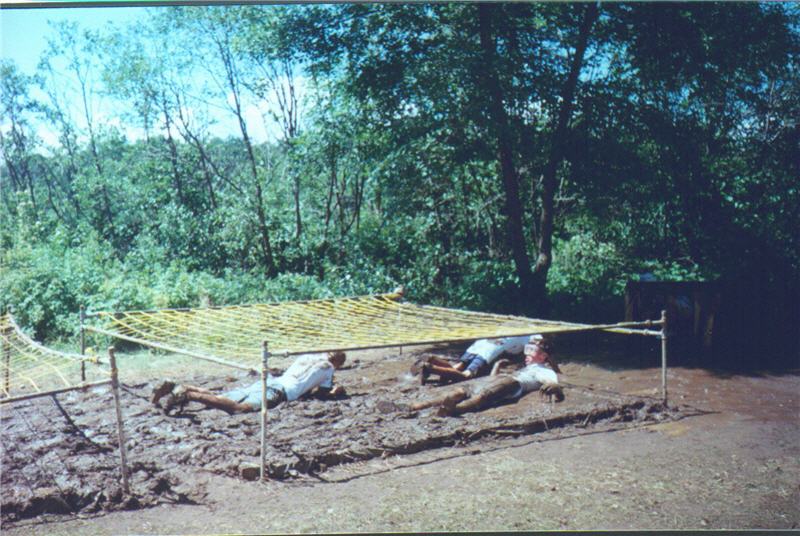 People on their stomachs crawling through the mud under netting