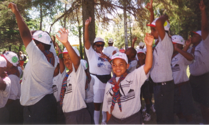 A group of scouts laughing and putting their hands up in front of trees