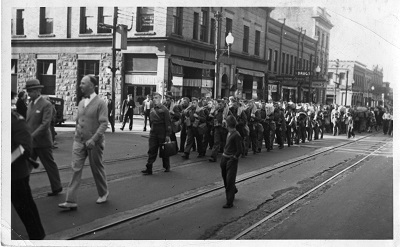 a parade of soldiers walks down the street lead by men in suits