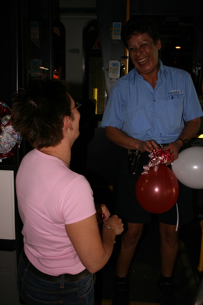 A person holding balloons facing the camera as a woman laughs with her back to it