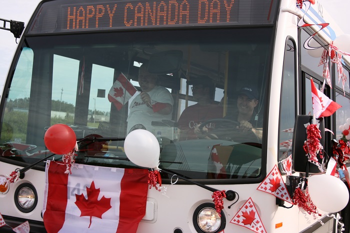 A bus that is decorated in red and white with Happy Canada Day on the front