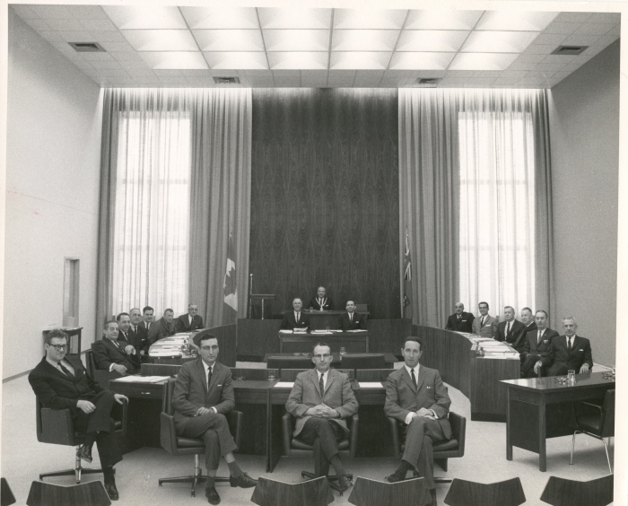 A group of people sitting around a squared off table in an official council chamber