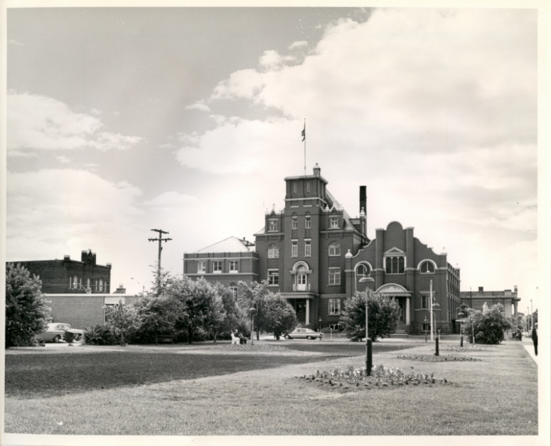 A black and white photo of a large brick building with a large lawn in front