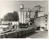 A black and white image of a grain elevator and railroad cars 