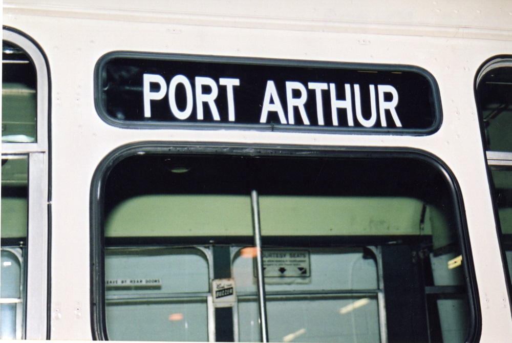 The door of a red and white trolley bus shown closed with the words Port Arthur above