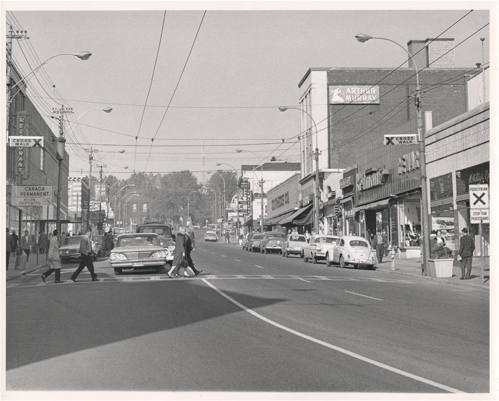 People driving cars and walking across the crosswalk down a busy street 