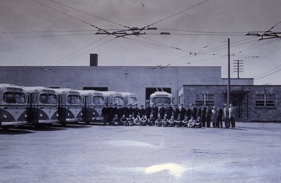 seven trolleys sitting idle in a parking lot awaiting use with their driver standing in front