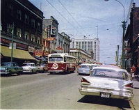 a red trolley going down a street lined with cars 