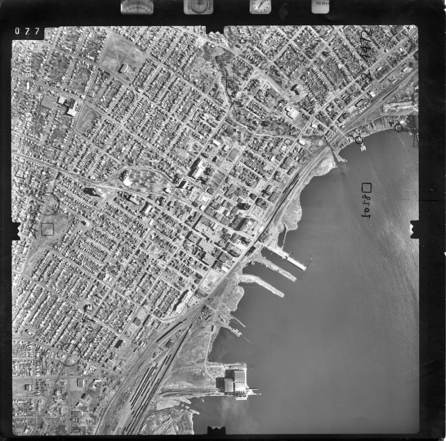 A black and white aerial photo showing the waterfront and surrounding area  