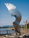 A silver statue in the shape of a wing sitting in front of water