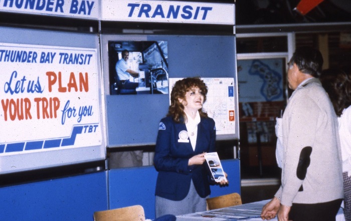 woman standing at a booth and holding a brochure up for another person.