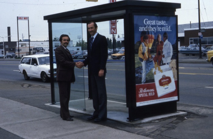 two men shaking hands in front of bus shelter.