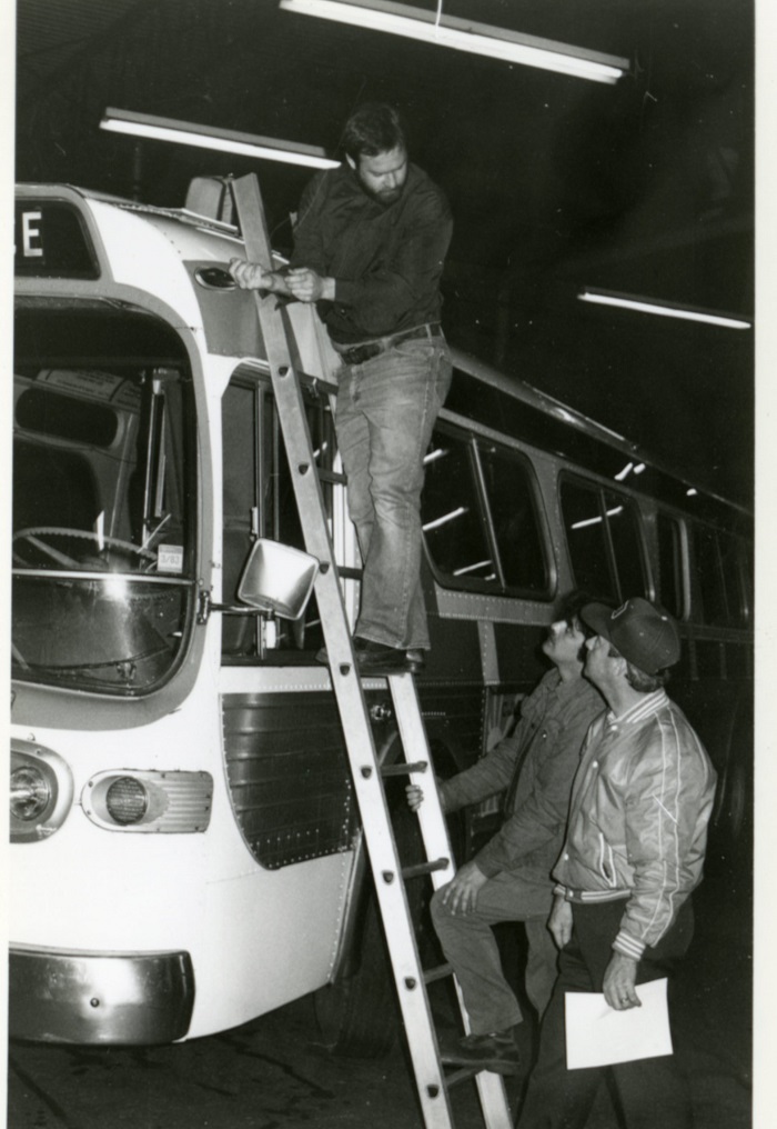 a person standing on a ladder that is leaning against a bus. 