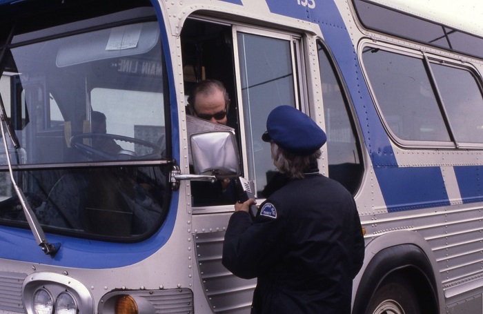 two bus drivers talking to each other through a bus driver's side window. 