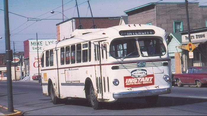 A white trolley with a red sign on the front travels down a street 