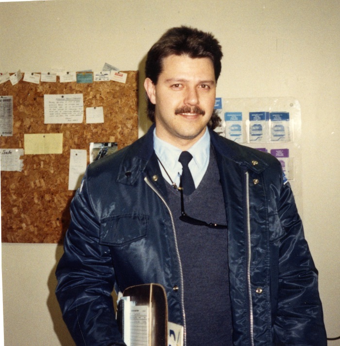 a man standing holding a clipboard and wearing a jacket smiling at the camera