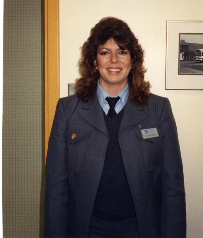 A woman with curly brown hair standing and smiling at the camera
