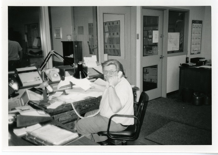 A man turning in his seat to look at the camera while on the phone in an office