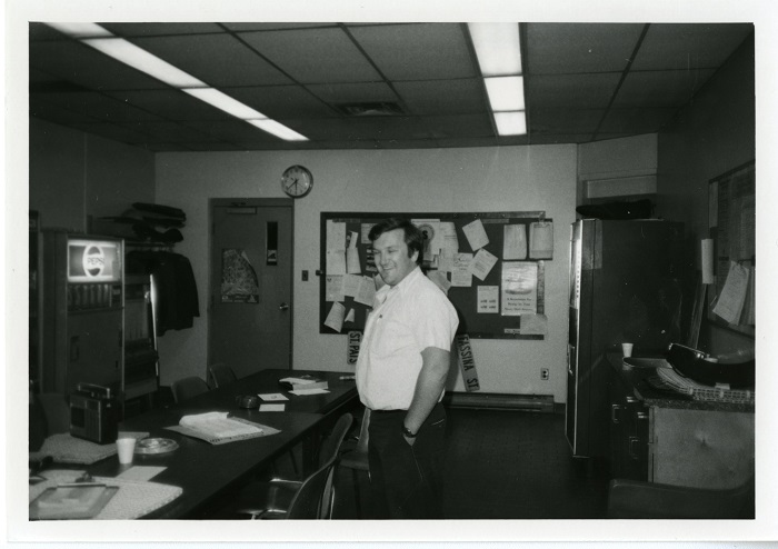 a man standing turned away but smiling back at the camera in an office