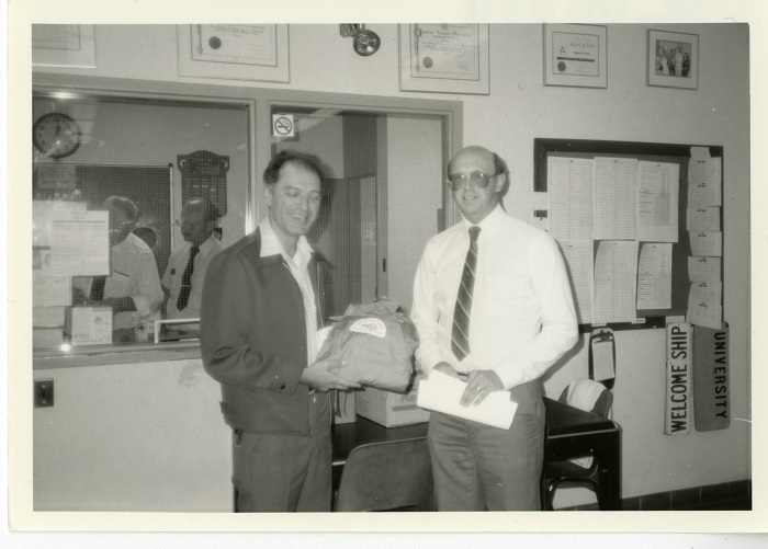 Two men standing beside each other with one man handing the other a shirt