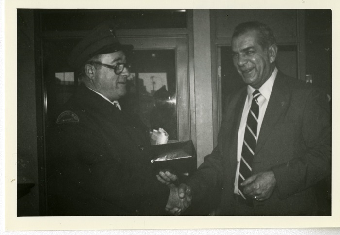 Two people shaking hands, while one holds something in his other hand