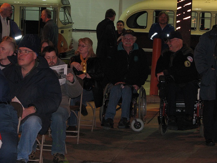 A group of people both seated and standing listen to a presentation