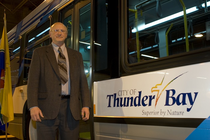 A man standing beside a bus with flags behind him in a garage 