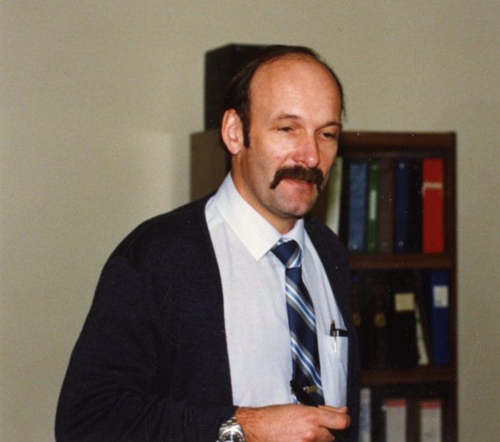 a man standing looking down wearing a blur cardigan and blue tie