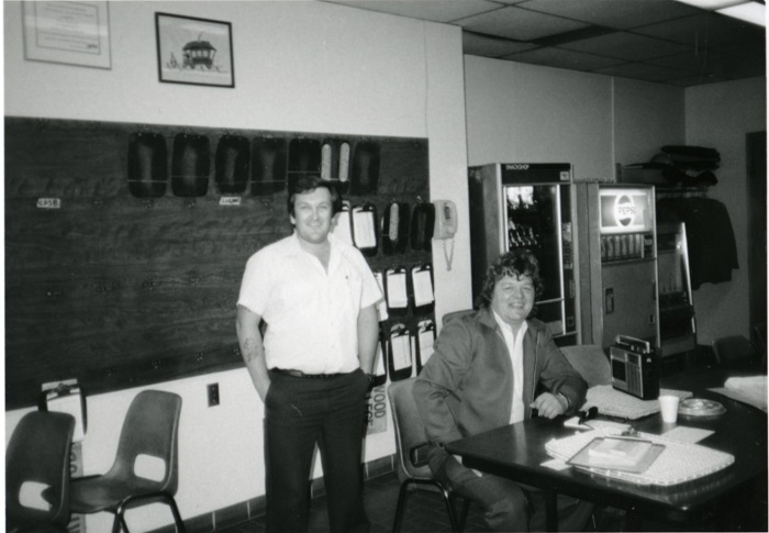 Two people, one sitting and one standing smiling for the camera in an office