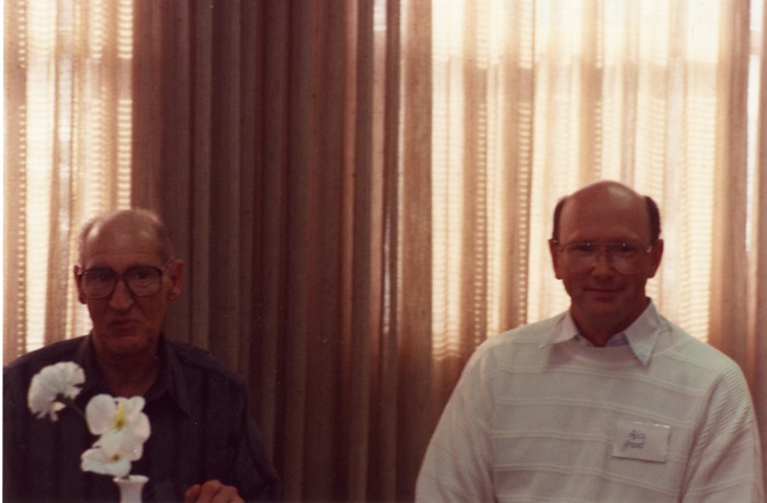 Two men sitting side by side and smiling at the camera