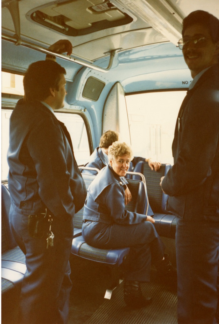 A group of transit employees sitting and standing on a bus looking out the back