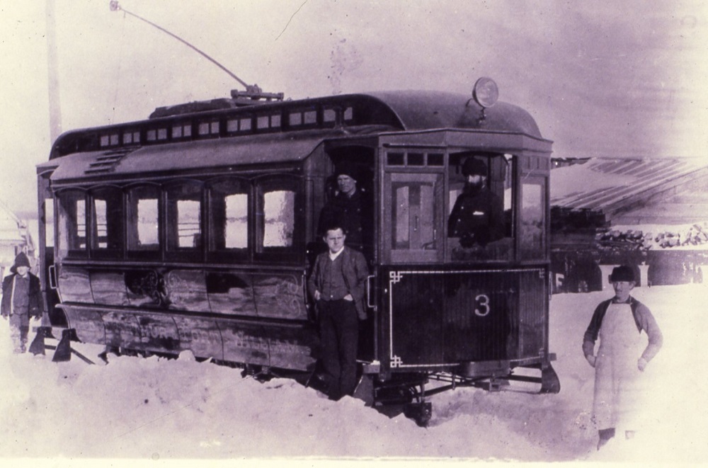 three men on a streetcar while one stands in front.