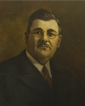 Mayor Ross sitting wearing a suit, with small glasses and has a moustache 