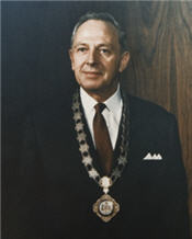 Mayor Reed standing wearing a suit, red tie and necklace 