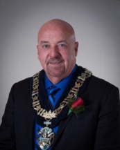 Mayor Keith Hobbs sitting in front of a grey background wearing a suit and large necklace