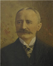 Mayor Ruttan sits wearing a black suit and has a large moustache