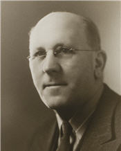 Mayor Booth sitting for a black and white photograph wearing a suit and small glasses