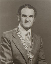 Mayor Saul Laskin wears a suit, stripped tie and a large necklace