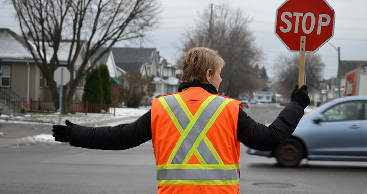 A photo shows a Thunder Bay crossing guard deploying a stop sign at a school crossing.