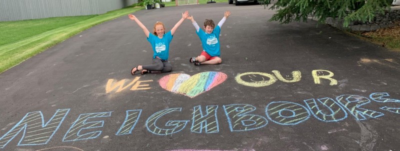 Kids write "We love our Neighbours" in chalk