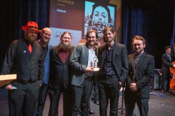 group of three men presenting an award to three band members on stage