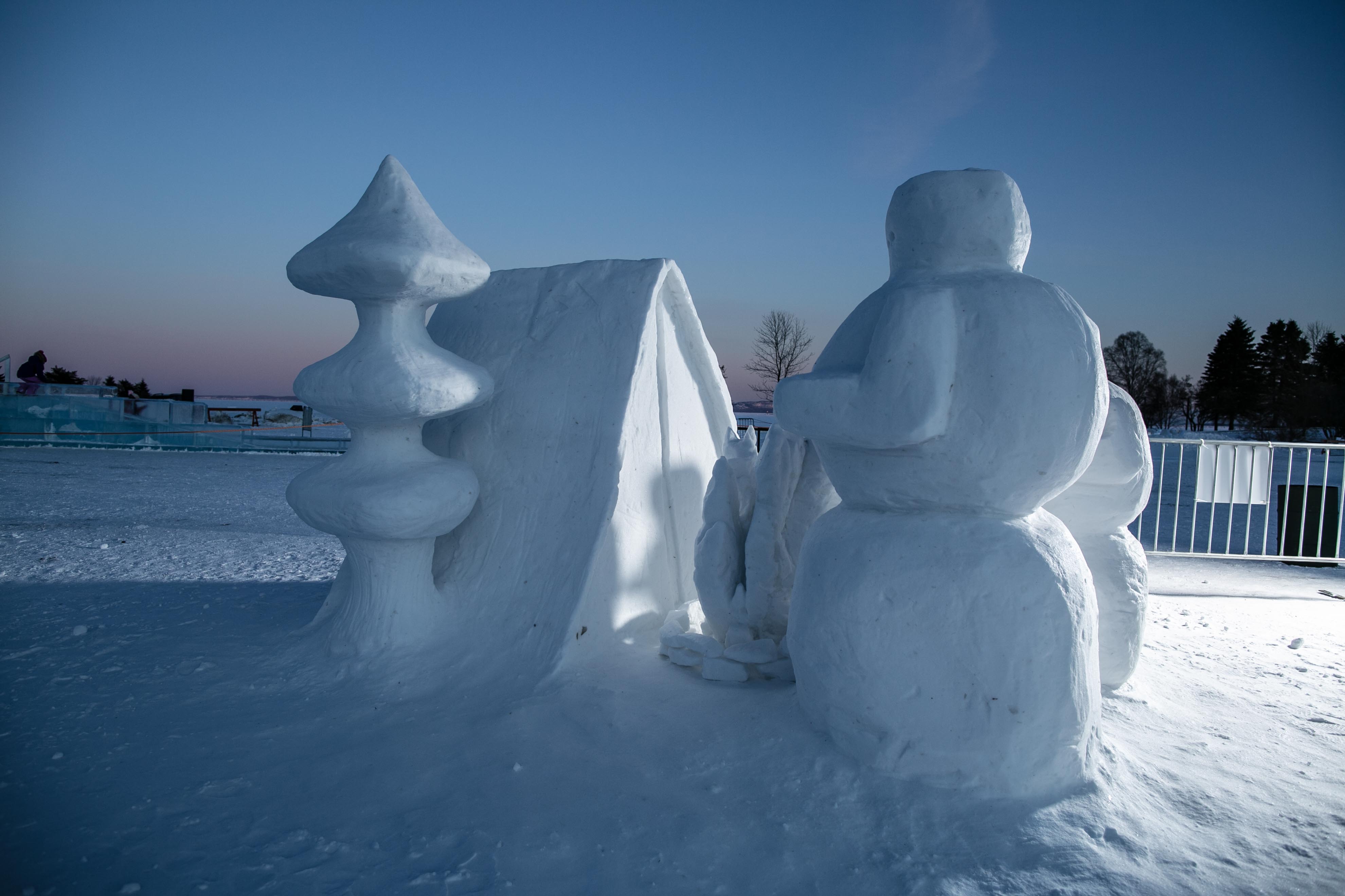 A snow sculpture of a family of snowmen camping