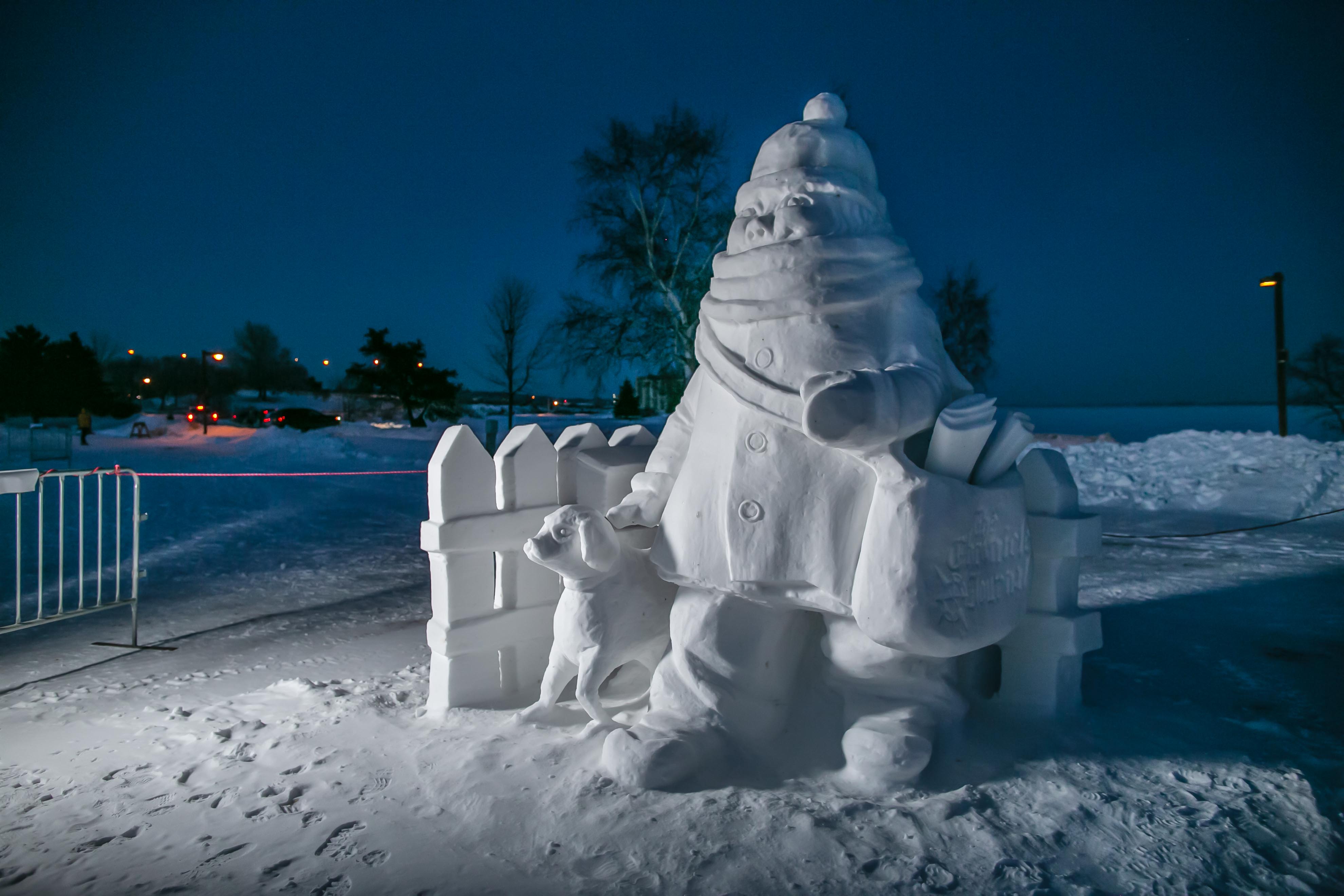 A snow sculpture of a young girl delivering Chronicle Journal newspapers with her dog