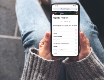 Graphic of person holding phone open to Report a Problem page of ThunderBay.ca