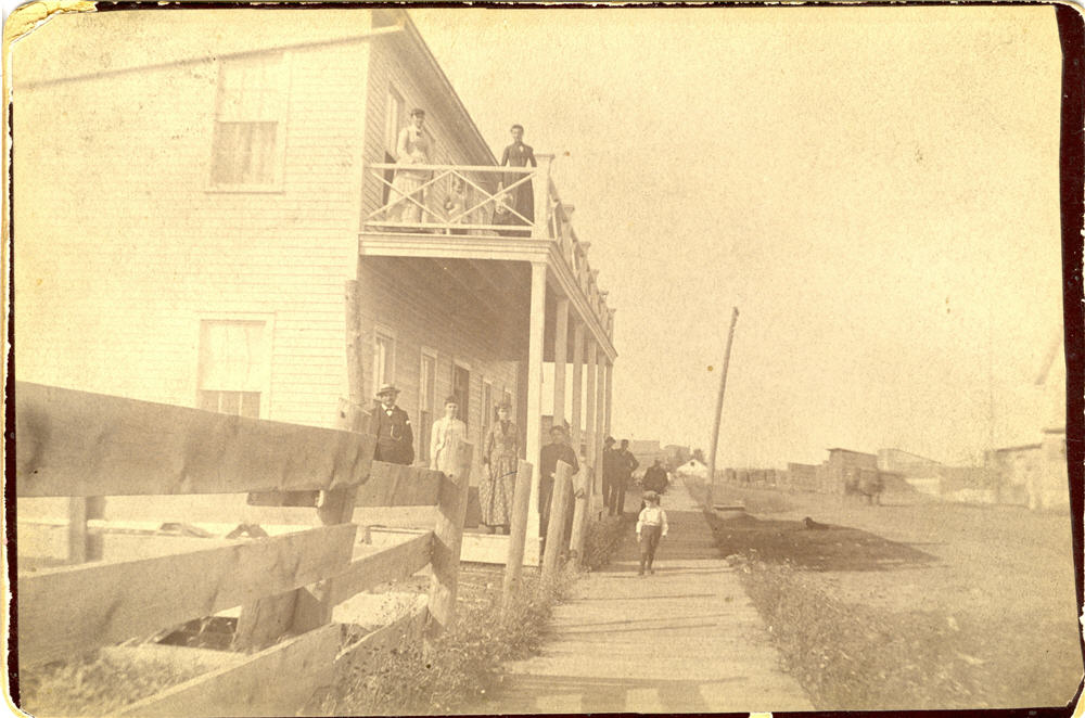 Multiple people standing on the street, and on the balcony of a building
