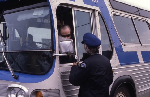 two bus drivers talking to each other through a bus driver's side window.
