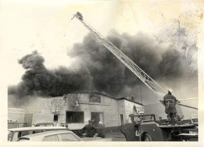 A fire truck with its ladder extended surrounded by firefighters fighting a fire