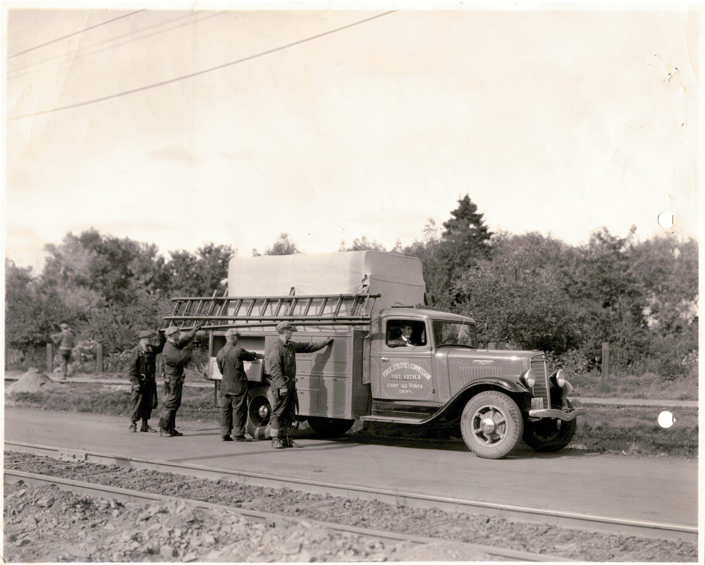 One man sitting in truck and four men standing at side of truck