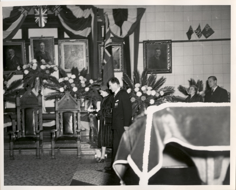 A group of people standing in front of chairs and flags inside a building